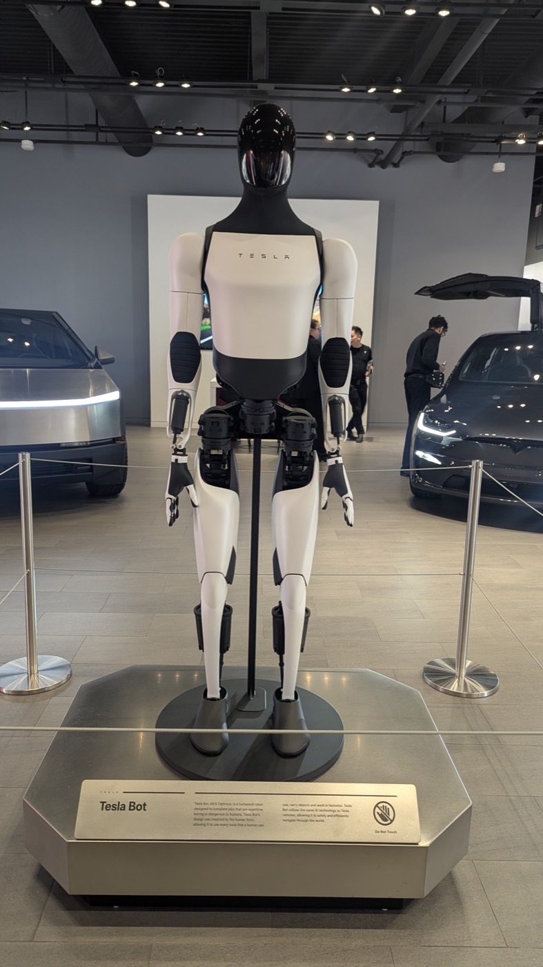 Tesla Optimus humanoid robot standing on display at a Tesla showroom